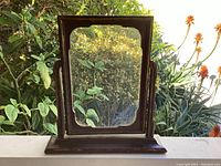 Front view of the wooden tilting swing frame with reflective original glass, placed outdoors showing the frame base and ornate carving details.