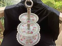 Three-tier porcelain serving stand with pierced edges and floral gold detailed design, angled view showing all tiers and central handle.