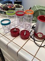 Six clear plastic containers with colored rims and two red blade attachments placed next to motor base.