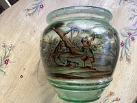 Front side of vintage green glass vase showing hand-painted hunting scene of a hunter and dogs near a tree.