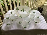 Punch bowl and 11 matching cups arranged on a tablecloth displaying hand-painted ivy design on frosted glass.