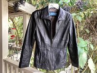 Front view of black leather jacket hanging outdoors, zippered with collar and front pockets visible