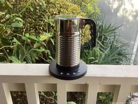Nespresso Aeroccino 4 electric milk frother and warmer on white surface outdoors, stainless steel milk container with black handle on black control base.