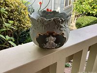 Image showing the bowl on an outdoor railing with visible floral sculpting and relief figure.
