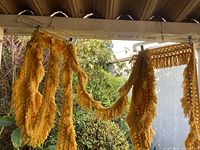 Bright yellow vintage boho fringe hanging from a hanger, showing long tassels and texture in natural light with outdoor background.