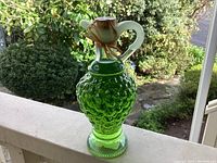 Front view of the green grape cluster glass cruet on table by window showcasing color and texture.