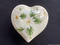 Heart-shaped trinket box top and sides showing white daisy flower decoration with embossed border on creamy porcelain.