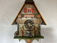 Front view of vintage Schmeckenbecher blacksmith cuckoo clock showing wooden chalet design, blacksmith figures, clock face and decorative details.