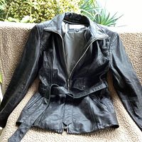Front view of black leather jacket with zip front, collar, side and breast pockets, and belt at waist.