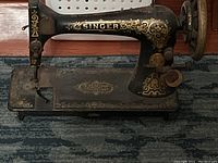 Close-up image of the black Singer sewing machine base showing gold floral designs and the "Singer" name in gold lettering