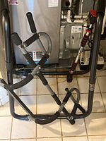 Free standing dip bar shown standing on floor with black padded grips and gray metal structure