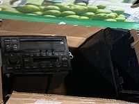 Front view of black car radio unit and black housing sitting in a box