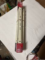 Photo of two white metal drawer slides bundled together with packaging showing product details