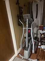 Full view of the elliptical machine positioned in a room near a door and guitars on the wall.