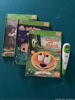 LeapFrog Tag reading pen and three storybooks laid out on a flat surface, pen on right side, books stacked with covers visible