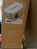 Side view of the orange box featuring image of mini projector with lens and support team contact info.