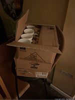 Three cardboard boxes stacked containing white ceramic coffee mugs wrapped in packing paper.