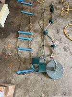 Rope ladder with blue plastic rungs, green plastic square swing seat, and round rope disk swing with green rings and chains laid out on concrete floor.