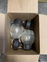 Two porch lights with crackle glass globes and oil rubbed bronze finish bases seen from above inside a cardboard box, showing textured glass and metal mounts.