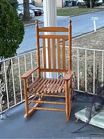 Full view of the wooden rocking chair showing the seat, backrest, armrests, and rockers on a porch.