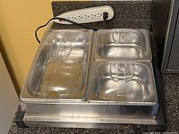 Full view of the electric 3 well food warmer with three stainless steel wells and clear lids, plugged in on a countertop.