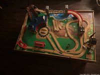 Top view of wooden train table showing detailed train tracks, bridge, roundhouse, storage drawers, and painted landscape surface.
