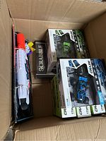 Box containing sealed Nerf Mega Big Rig dart blaster, Scrabble board game, and Power Craze RC vehicles