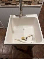 White utility sink with stainless steel faucet and extra plumbing parts placed inside basin.