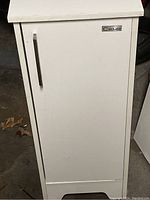 White cabinet with single door and metal handle, shows slight dirt and wear
