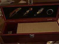Photo showing open wooden wine box with compartment spaces for bottles and wine opening tools securely held in the lid.
