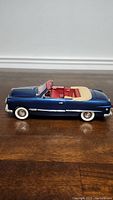 Side view of the 1949 Ford 1/18 scale model, showing the dark blue body and cream convertible top down with red interior seats.