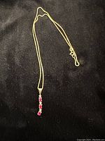Full view of the gold chain and ruby pendant on a dark fabric background.