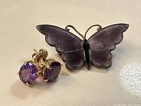 Front view of 14k gold amethyst stud earrings and butterfly brooch with purple wings and black body, showing design details and gem color.