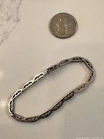 White gold bracelet next to a quarter for scale showing openwork design and black diamond accents.