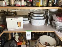 Shelf with boxed Wine Enthusiast double wall beer tumblers, CorningWare baking dishes in blue cornflower pattern, and a floral patterned CorningWare baking dish.