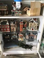 Photo of shelves with various Christmas village houses, including grocery store and lighted houses with electrical cords.