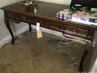 View of full wooden desk with carved legs and three drawers, showing overall wear and scratches.