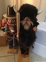 Partial grouping showing buffalo guard nutcracker with faux fur and horns alongside cowboy and other figures in background