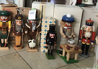 View of seven wooden nutcracker figures in various costumes arranged in front of original boxes.
