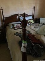 Photo showing tall, carved wooden bed frame post with a tag labeled '212' and dimensions '55x60x84'. Background includes the headboard and mattress with pillows and bedding.