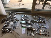 Full lot of assorted silver and stainless steel flatware on floor with natural light