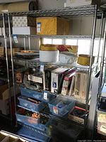 Full view of a metal wire storage rack on wheels with four shelves filled with various boxes and containers (contents not included).