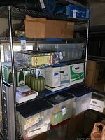 Four-shelf metal storage wire rack on wheels with various boxes and containers placed on shelves (contents not included in sale).