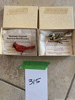 Both brooches in original patterned cream boxes labeled “cardinal” and “meadowlark”