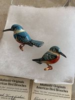 Two bird brooches front view on white padding with species cards beneath