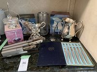 Full view of lot items including Waterford glasses, silver plated sauce warmer, pitcher, crystal dish, and cutlery set with original boxes.