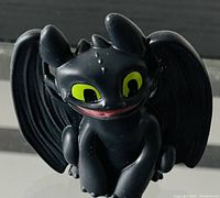 Front close-up of the small black bat toy figure with large green eyes and a smiling mouth, showing the details on the wings and head.