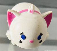Close-up front view of small white vinyl Disney Tsum Tsum toy featuring blue eyes, pink nose, pink inner ears, and black whiskers shaped as Marie the cat.
