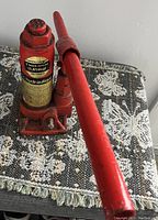 Red hydraulic bottle jack lift placed on patterned surface showing handle and lifting unit.