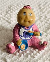 Photo of a small Cabbage Patch PVC toy figurine in pink pajamas holding a blue bowl and spoon, showing some paint wear.